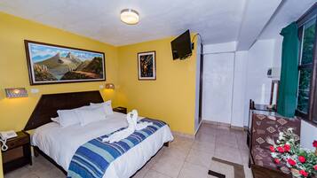 A hotel room with a bed, a nightstand, a telephone, a painting on the wall, a television, and a window with curtains.
