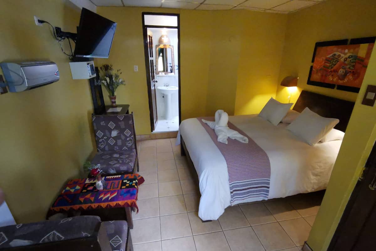 A hotel room with a bed, a desk, a chair, a television, and a bathroom visible through an open door.