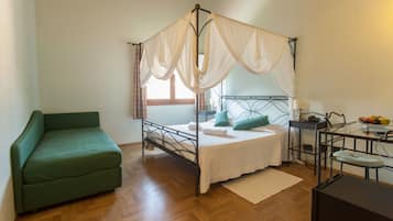 A room with a four-poster bed, a green sofa, a small table with a lamp, and a fruit bowl.