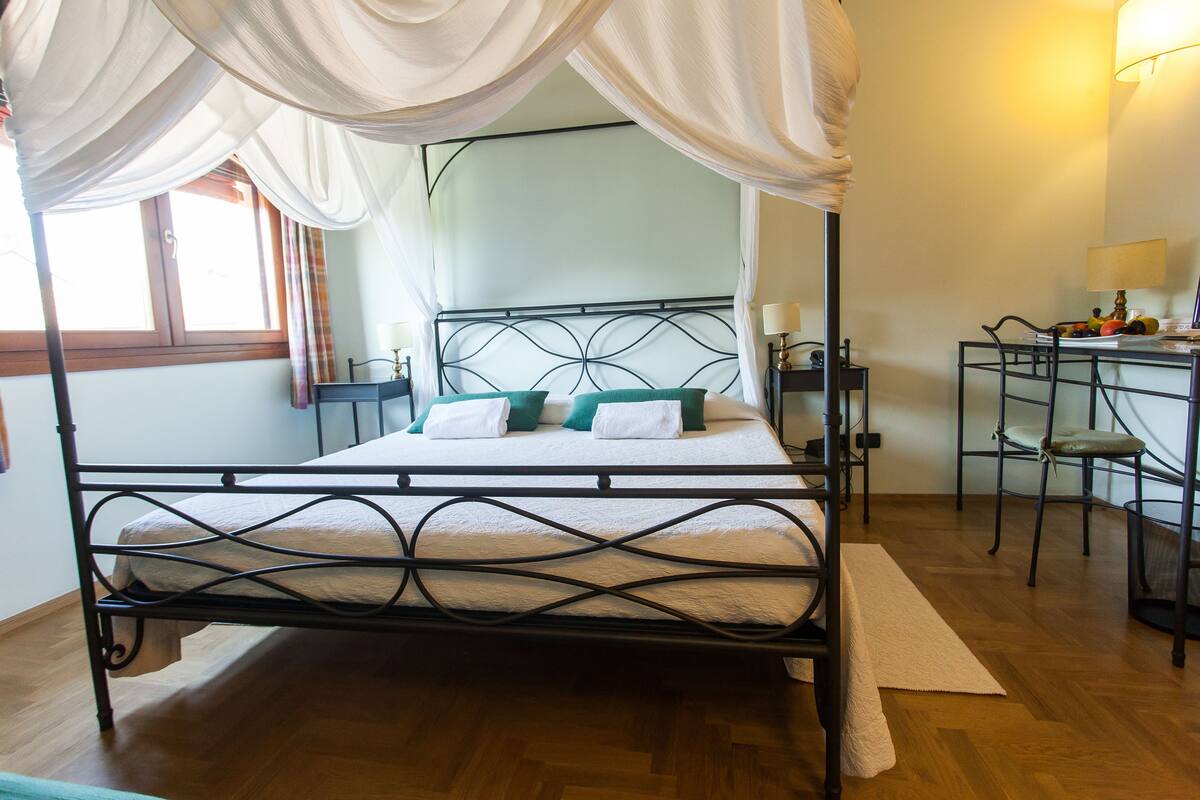 A four-poster bed with a canopy, a desk with a chair, and a nightstand with a lamp.