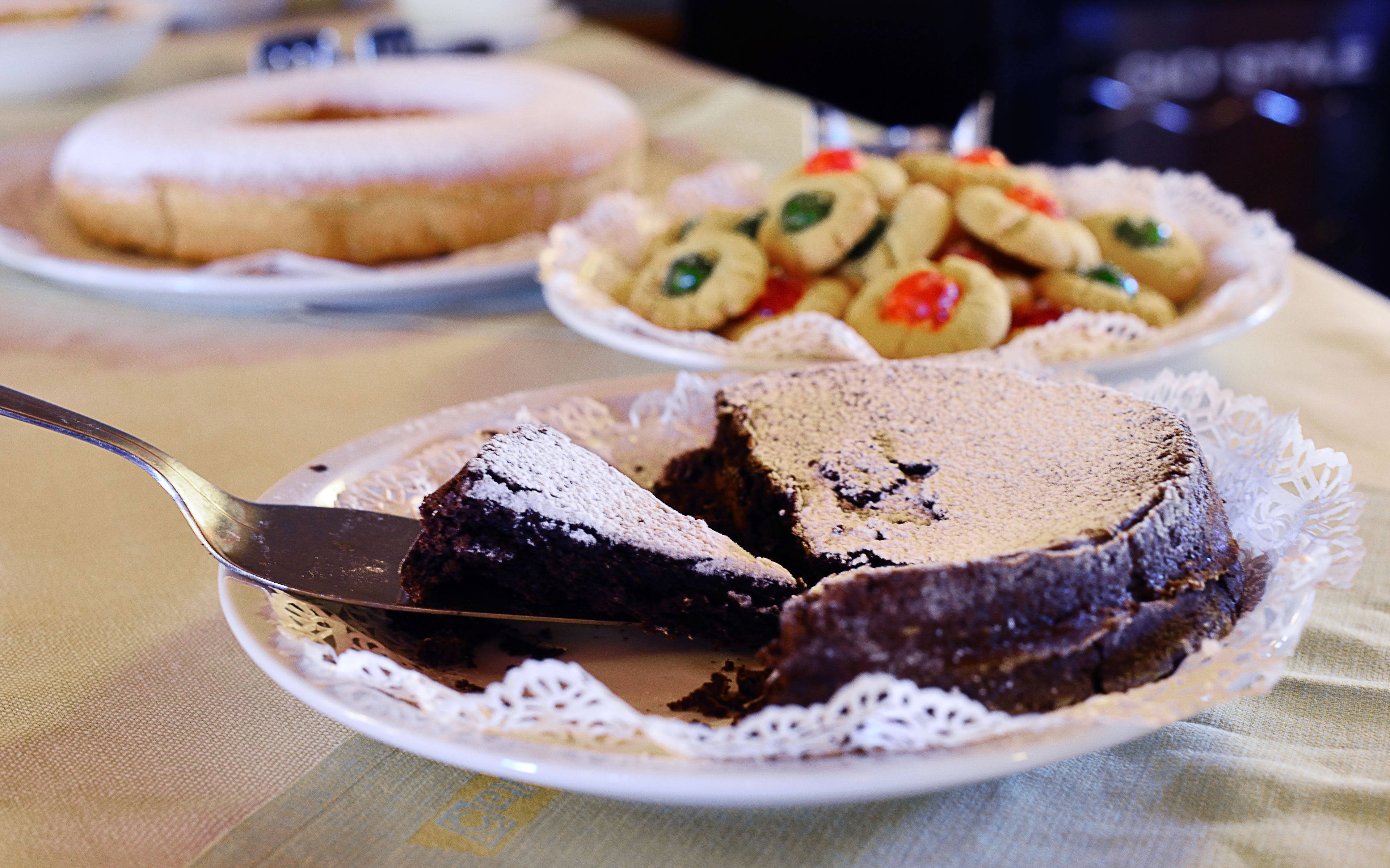 Un pastel con una porción cortada sobre un plato con un mantel de encaje, un donut y un plato de galletas sobre un mantel.