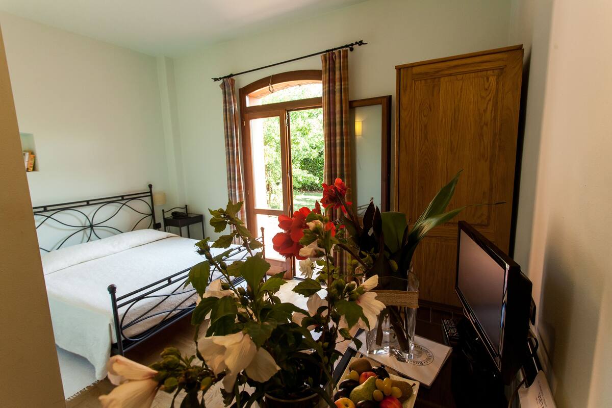 A bedroom with a bed, a desk with a computer, a window with curtains, and a door.