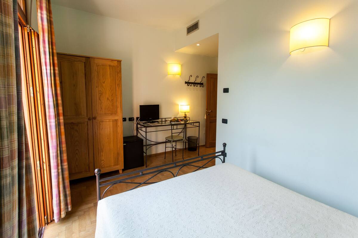 A bedroom with a bed, wooden wardrobe, desk, chair, and a television.