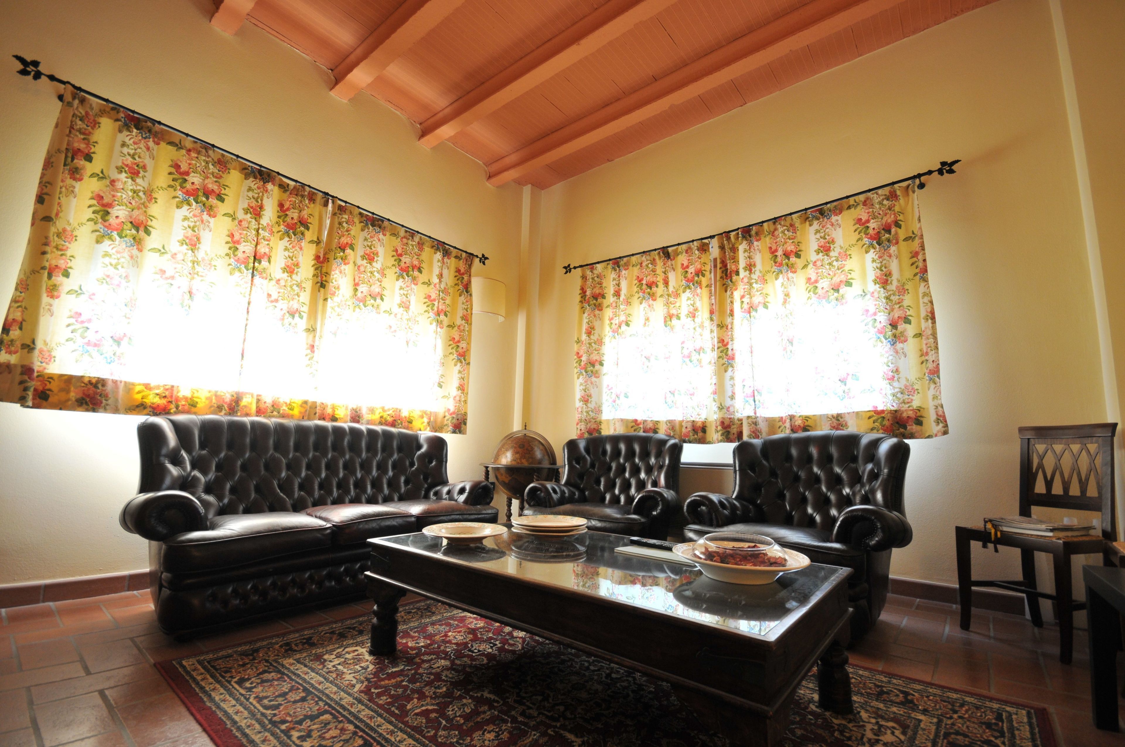 Una sala de estar con un sofá de cuero negro, una mesa de centro y cortinas con motivos florales.