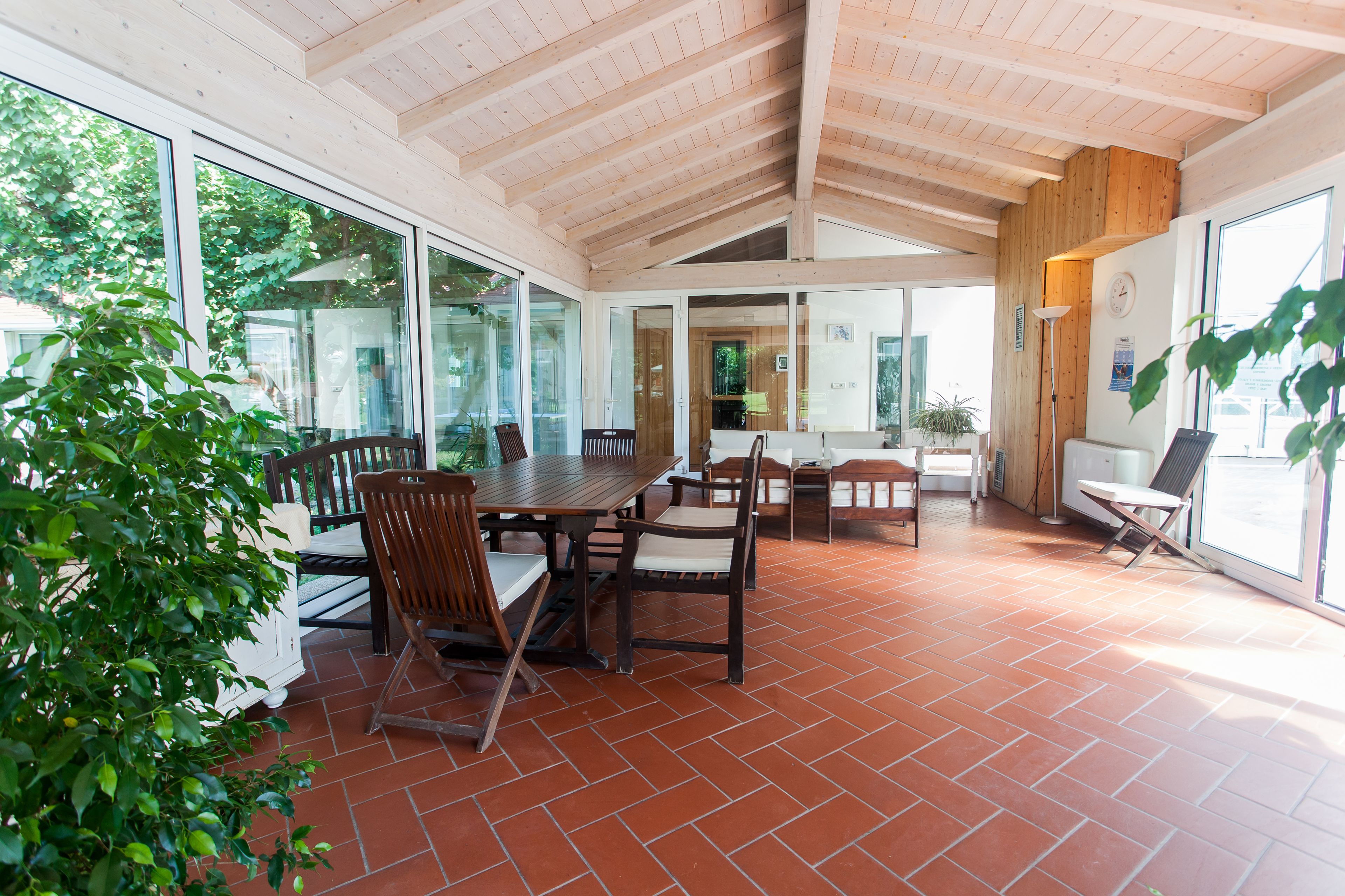 A spacious patio with a wooden table and chairs, large windows, and a tiled floor.