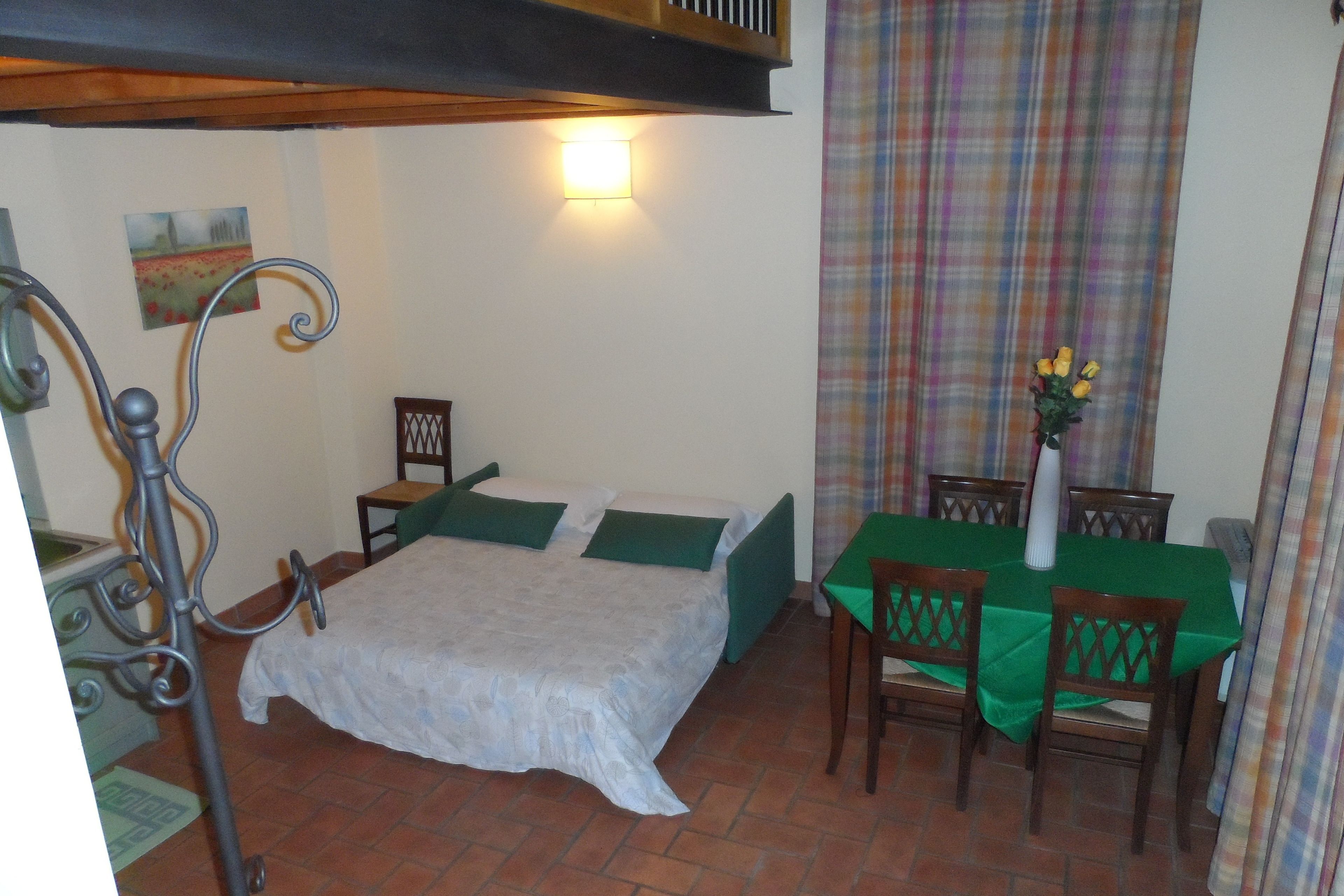 A small, cozy room with a bed, a dining table with chairs, and a wall-mounted light.