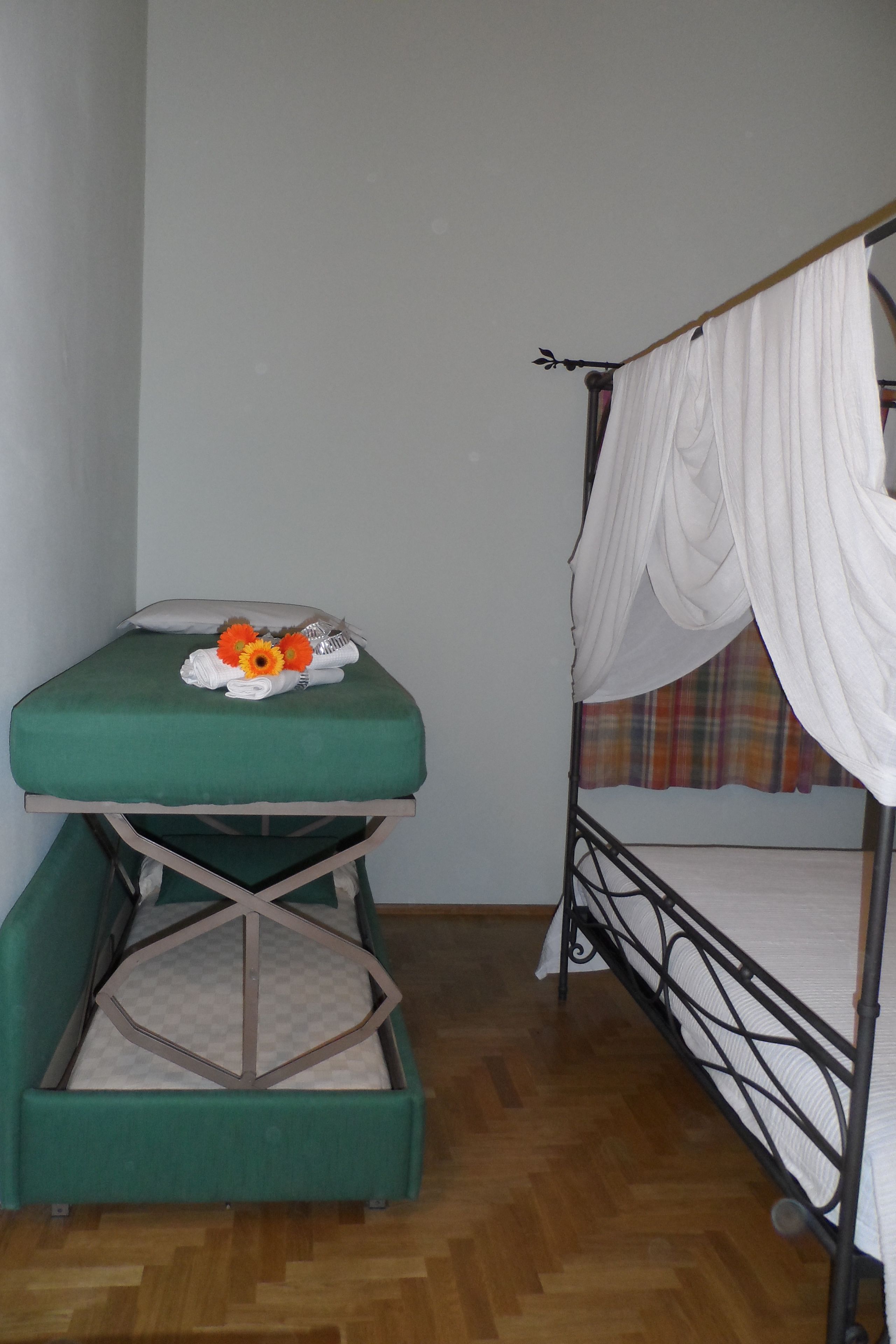 Una habitación con una cama litera, un sofá cama verde y una pequeña mesa con un arreglo floral.