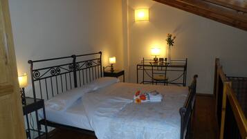 Una cama bien hecha con una colcha floral, una mesita de noche con una lámpara y una pequeña mesa con un jarrón de flores.