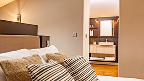 Een slaapkamer met een bed, kussens, een nachtkastje en een zichtbare badkamer door een geopende deur.