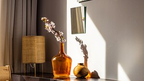 Een donker houten tafel met een geweven lamp, een glazen vaas met bloemen en een kleine houten schaal.