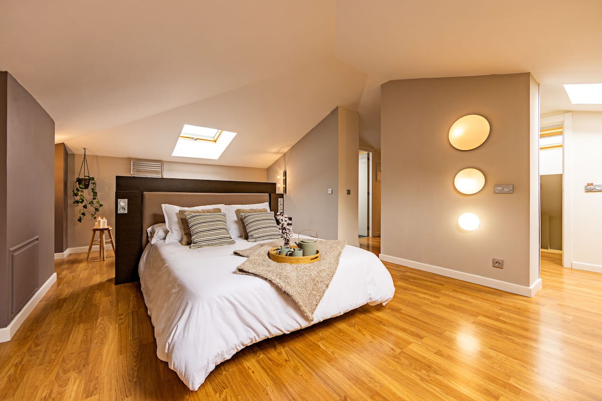 Quarto com cama grande, claraboia, piso de madeira e design moderno na parede.