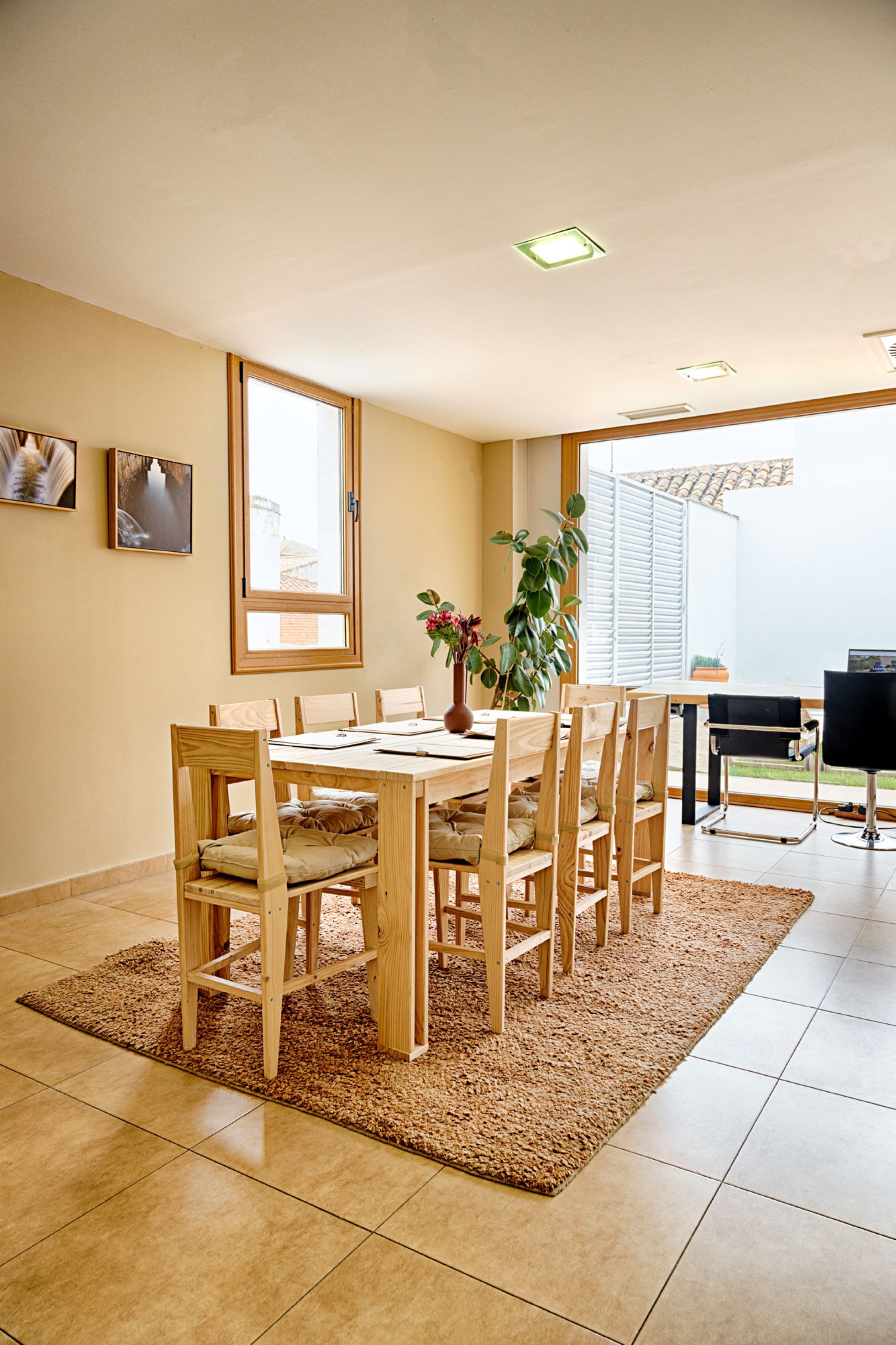 A dining area with a wooden table and chairs, a rug, and a window with blinds.