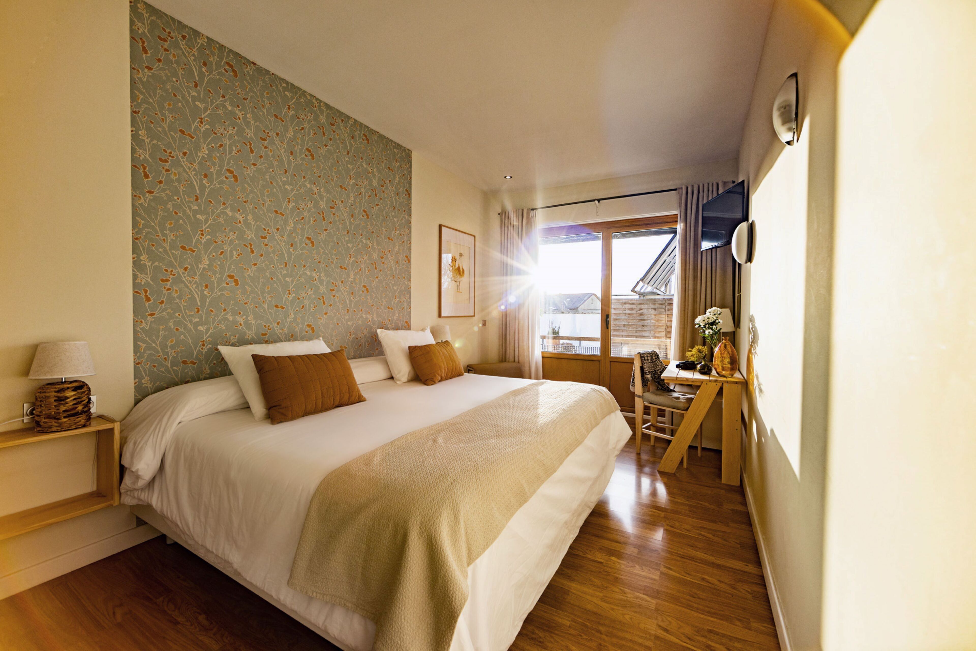 Une chambre avec un grand lit, un plancher en bois, un bureau avec une chaise et une fenêtre avec des rideaux.