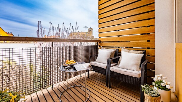 Een balkon met houten vloer, rieten meubels en een kleine tafel met een fruitschaal.