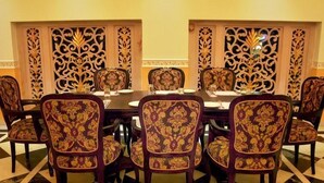 Une salle à manger élégante, avec une table ronde, des chaises richement décorées et des panneaux muraux décoratifs.