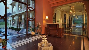Un hall d’hôtel comprenant un comptoir d’accueil, un vase décoratif et une vue sur la façade de l’immeuble.