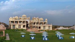 Un grand bâtiment imposant, doté de nombreux balcons et d’une pelouse bien entretenue, agrémentée de tables et de parasols.