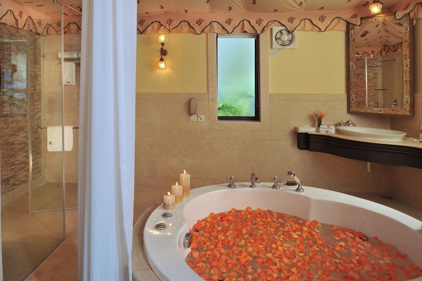 A bathroom with a large bathtub filled with rose petals, a glass shower enclosure, and a vanity with a mirror and sink.