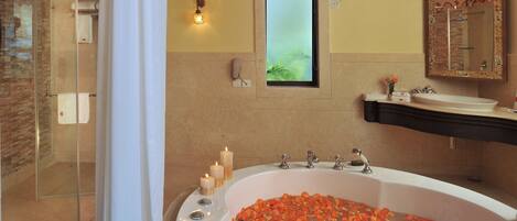 A bathroom with a large bathtub filled with rose petals, a glass shower enclosure, and a vanity with a mirror and sink.
