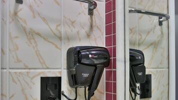 A bathroom with a hairdryer mounted on the wall, a towel rack, and toiletries on the counter.
