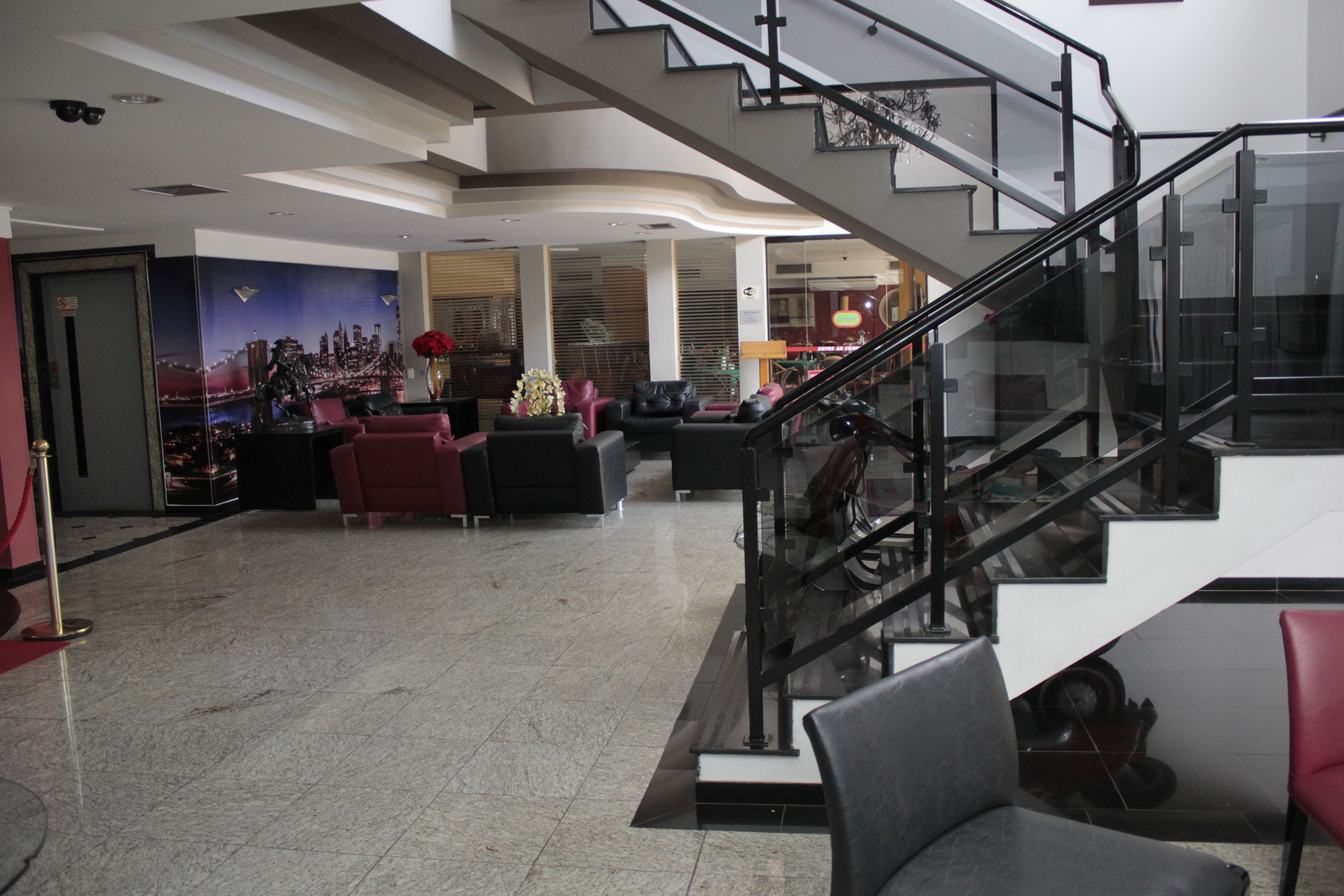 Um hall amplo com piso de mármore, escada com guarda-corpo de vidro e área de estar com sofás de couro.