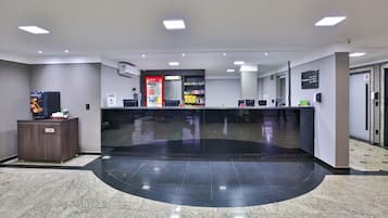 Zona de recepción de hotel con mostrador, refrigerador de Coca-Cola, máquina expendedora y cartel que indica prohibido fumar.