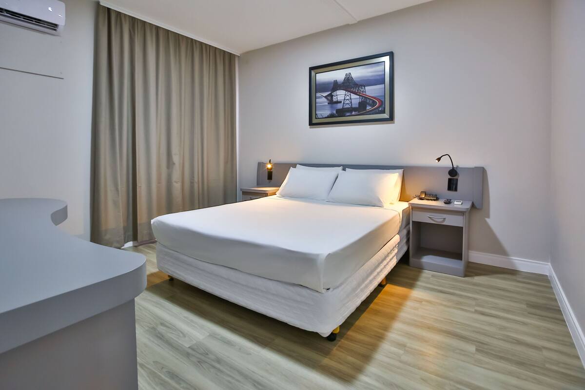A modern hotel room with a large bed, a desk, and a nightstand.