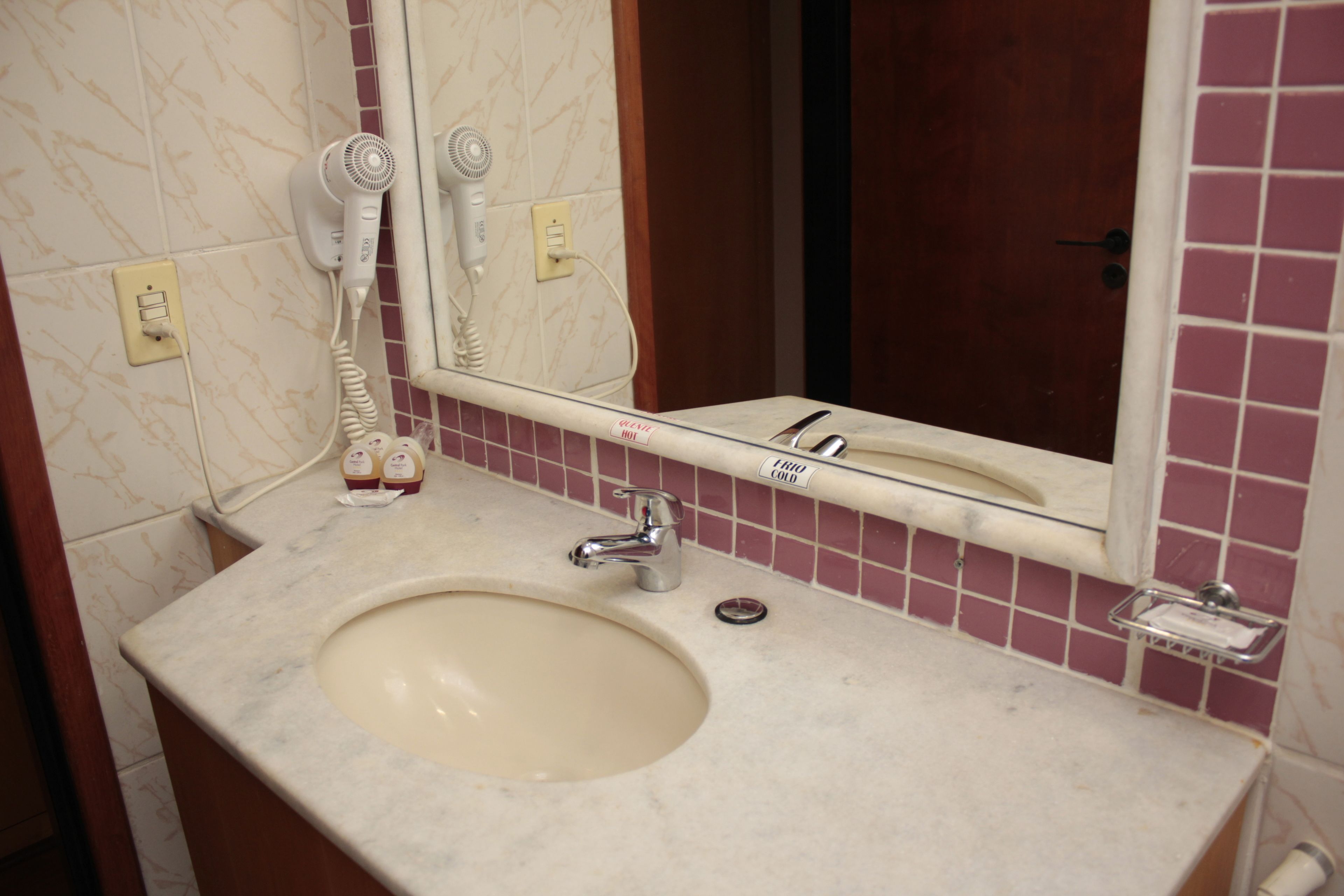 A bathroom with a sink, a mirror, and a hairdryer on the wall.