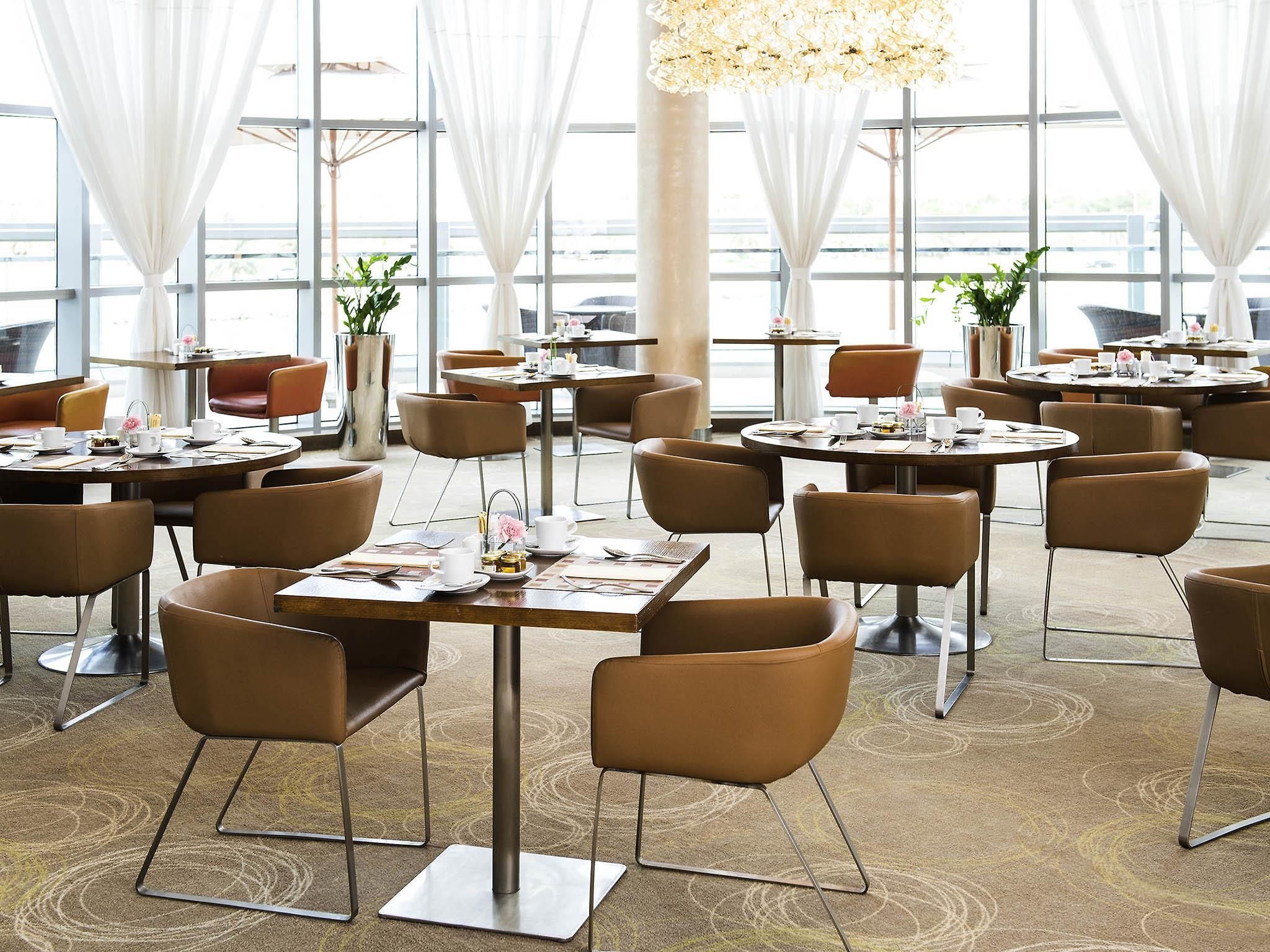 A modern dining area with round tables, brown chairs, and large windows.