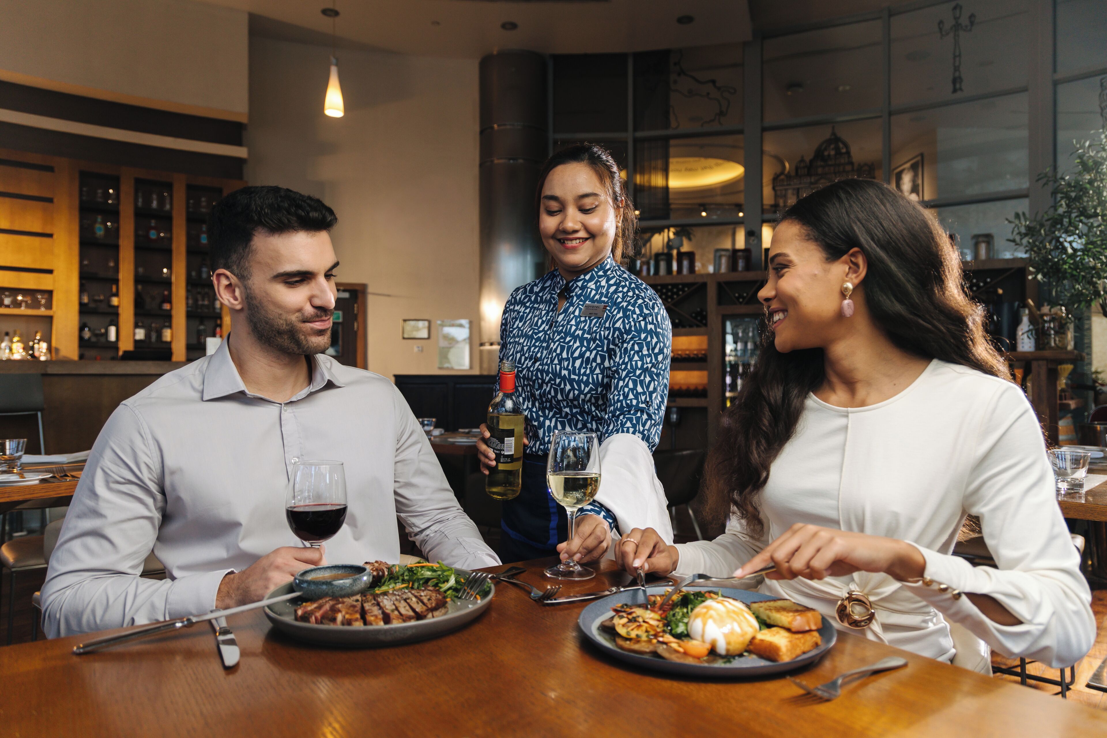 Een restaurantinterieur met een houten tafel, wijn glazen en een fles wijn.