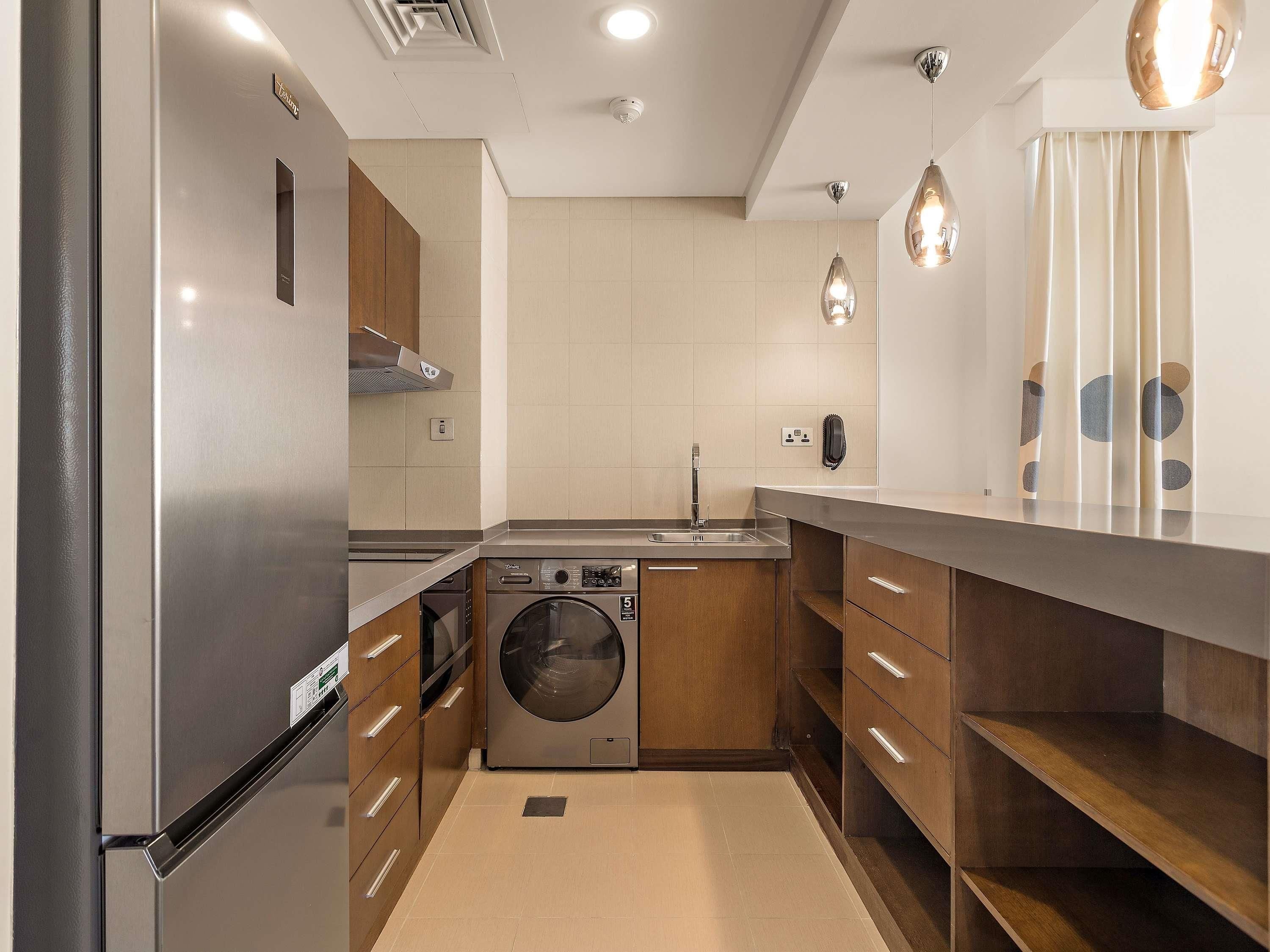 A modern kitchen with stainless steel appliances, a built-in washing machine, and wooden cabinets.