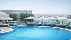 Une piscine sur le toit, dotée de chaises longues et de parasols, et offrant une vue panoramique sur la ville.