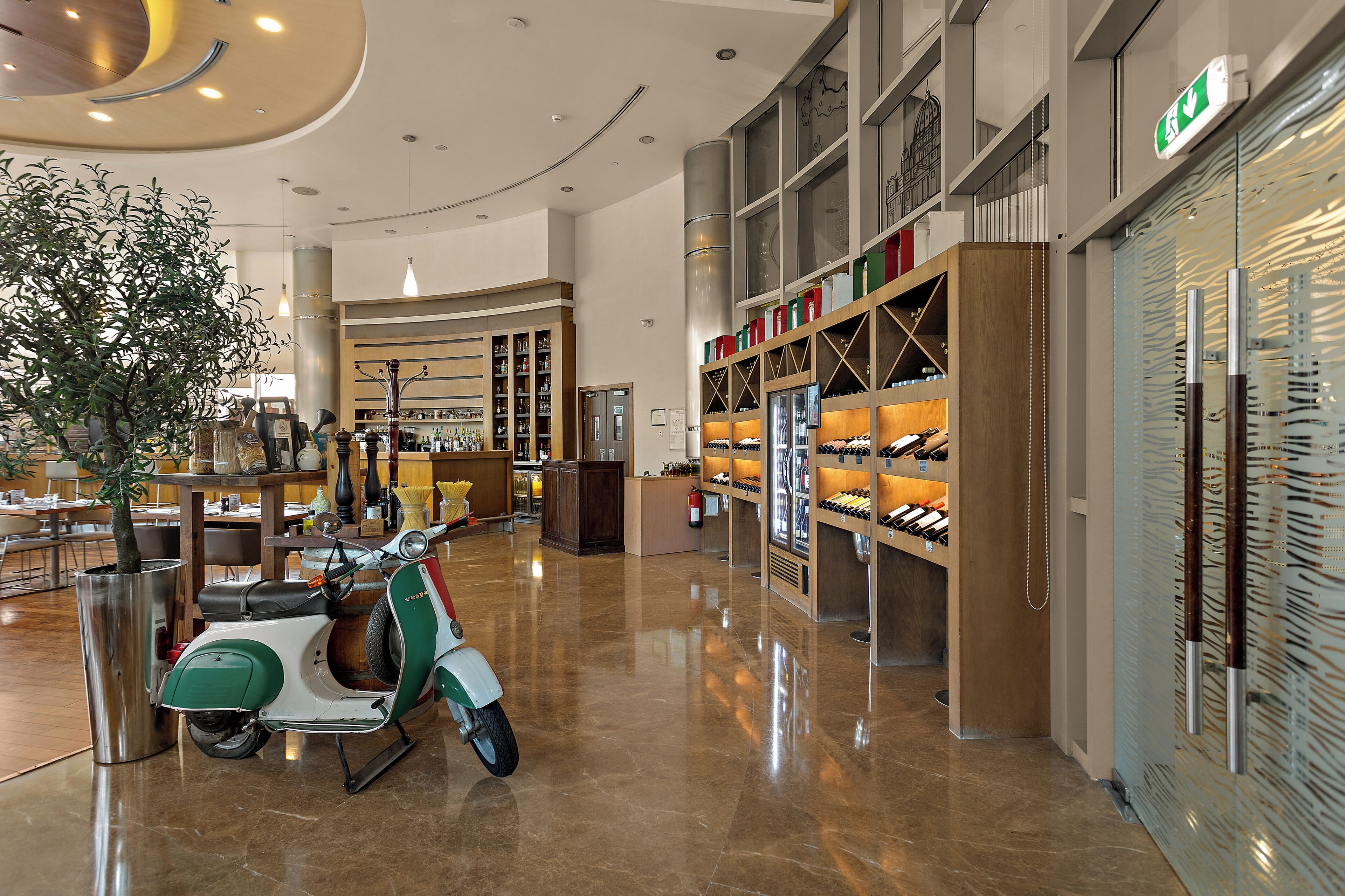 Un vestíbulo amplio con un scooter verde y blanco, un árbol grande y almacenamiento para vino.
