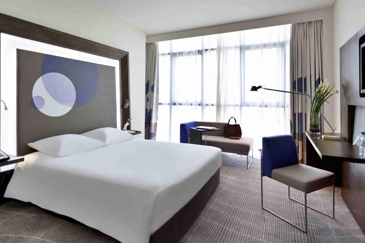 A hotel room with a large bed, a desk, a chair, a TV, and a window with curtains.