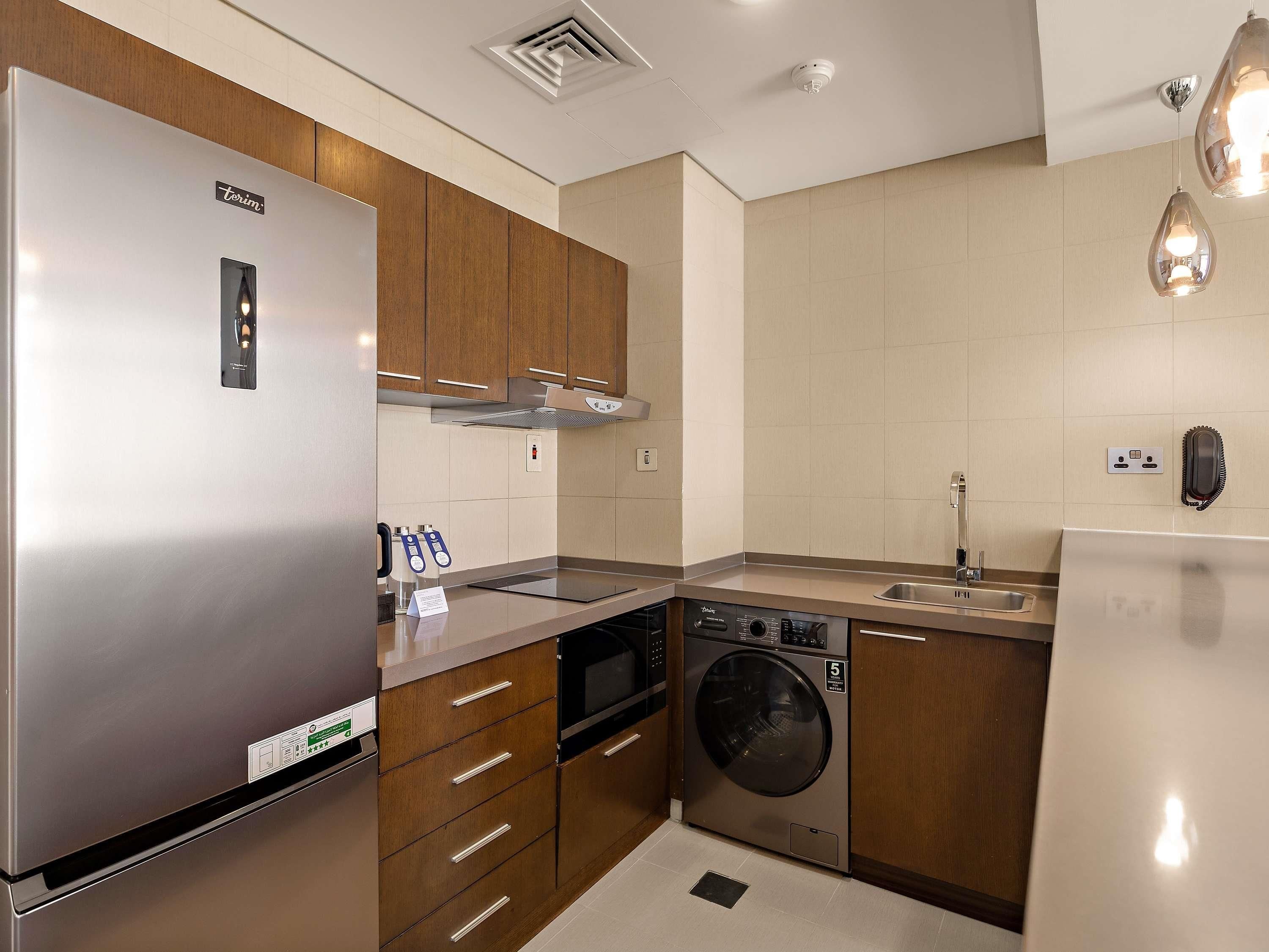 A modern kitchen with stainless steel appliances, wooden cabinets, and a built-in washer and dryer.