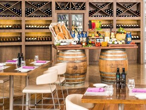 Ein Restaurant mit Holzfässern als Tischen, Weinflaschen in Regalen und einer Auswahl an Speisen und Getränken hinter der Bar.