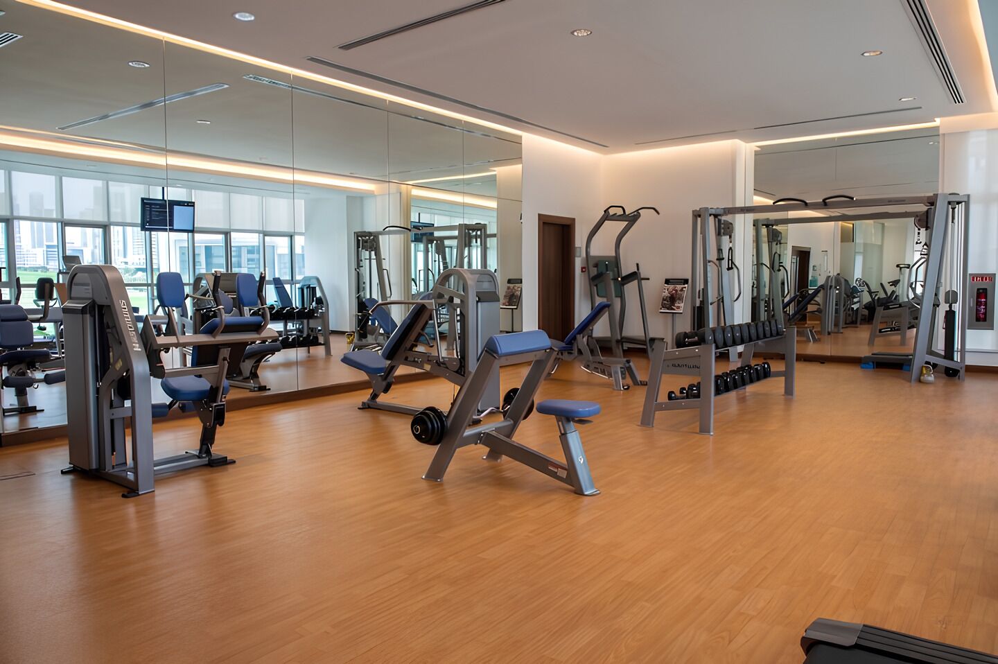 A gym with various exercise equipment, large mirrors, and wooden flooring.