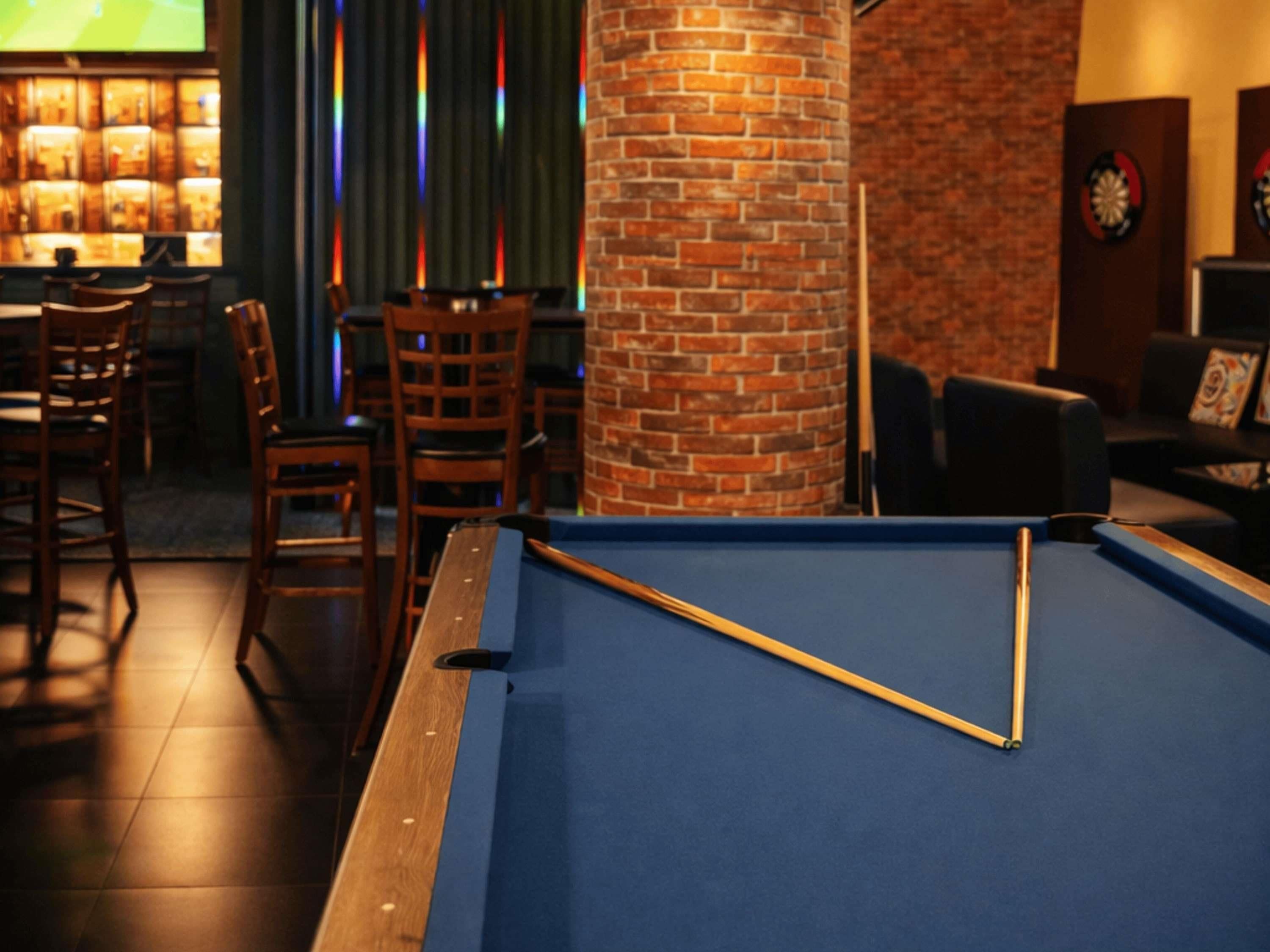 A pool table in a room with a brick column, wooden chairs, and a dartboard.