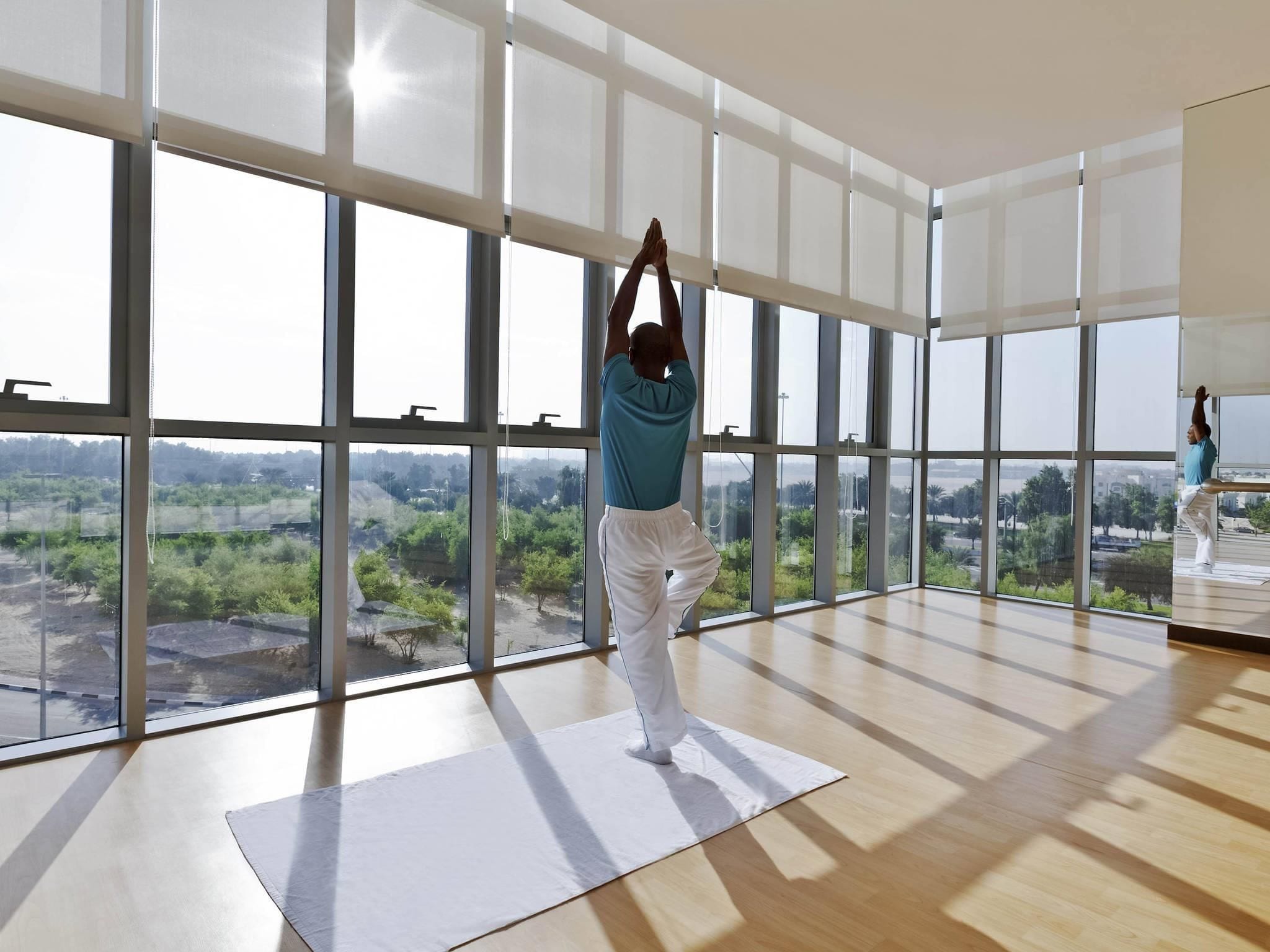 A spacious room with large windows, a yoga mat, and a person performing a yoga pose.