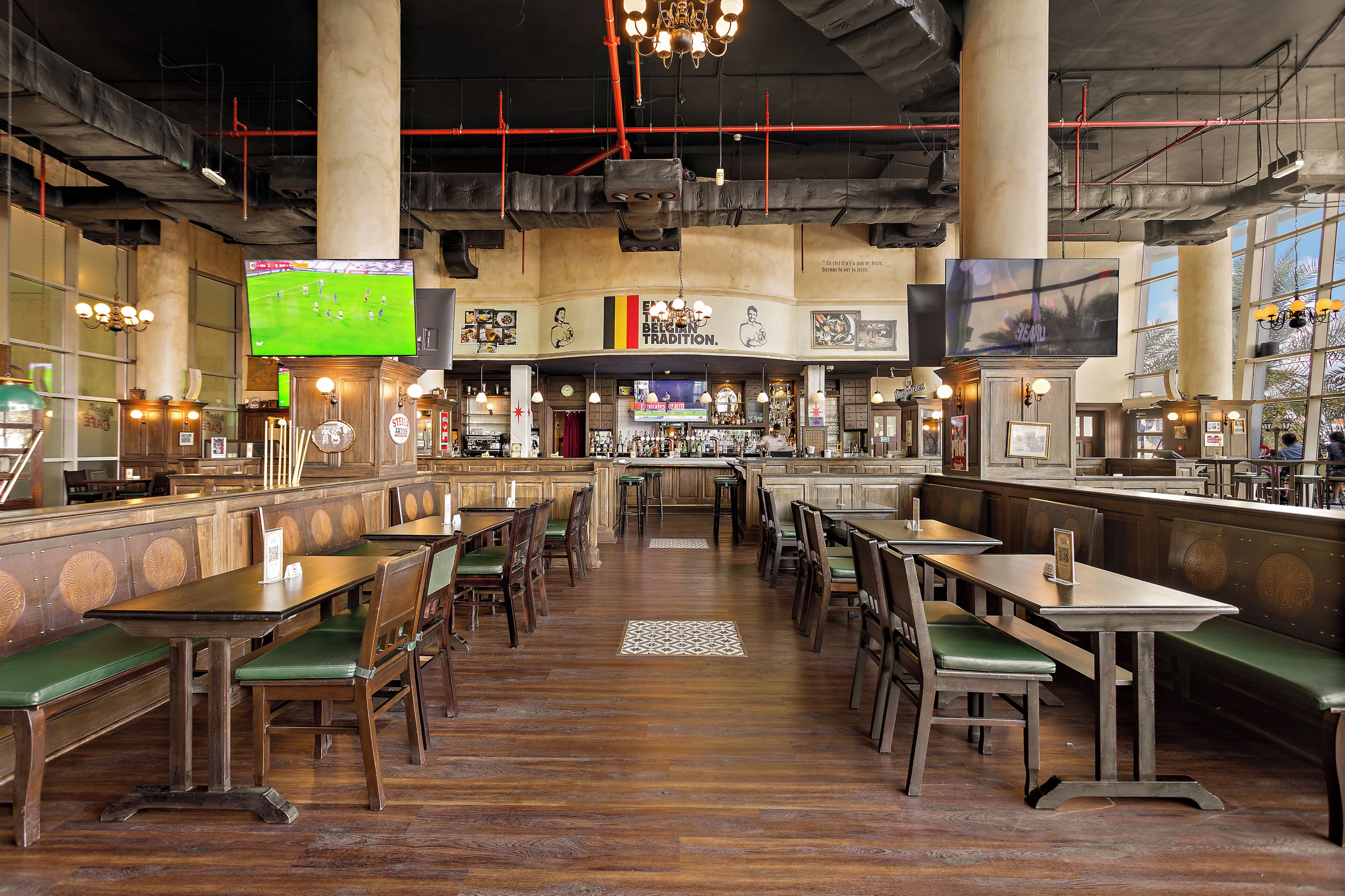 Un ristorante con tavoli di legno e panche imbottite verdi, un'area bar e ampie finestre.