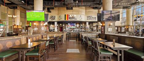 Un ristorante con tavoli di legno e panche imbottite verdi, un'area bar e ampie finestre.