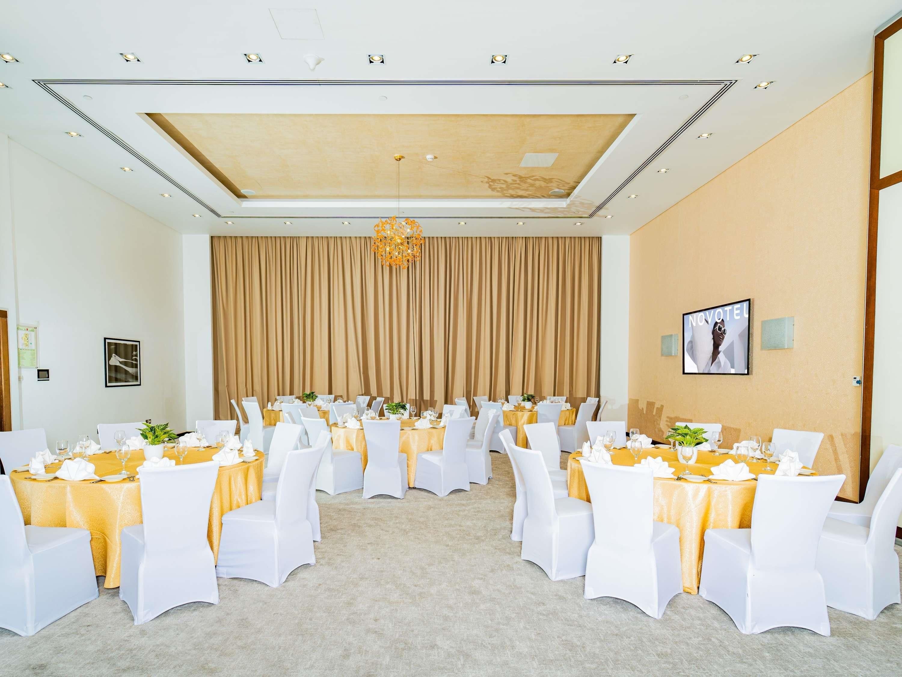 Un salón de conferencias con mesas redondas, sillas blancas y un fondo de cortina color beige.