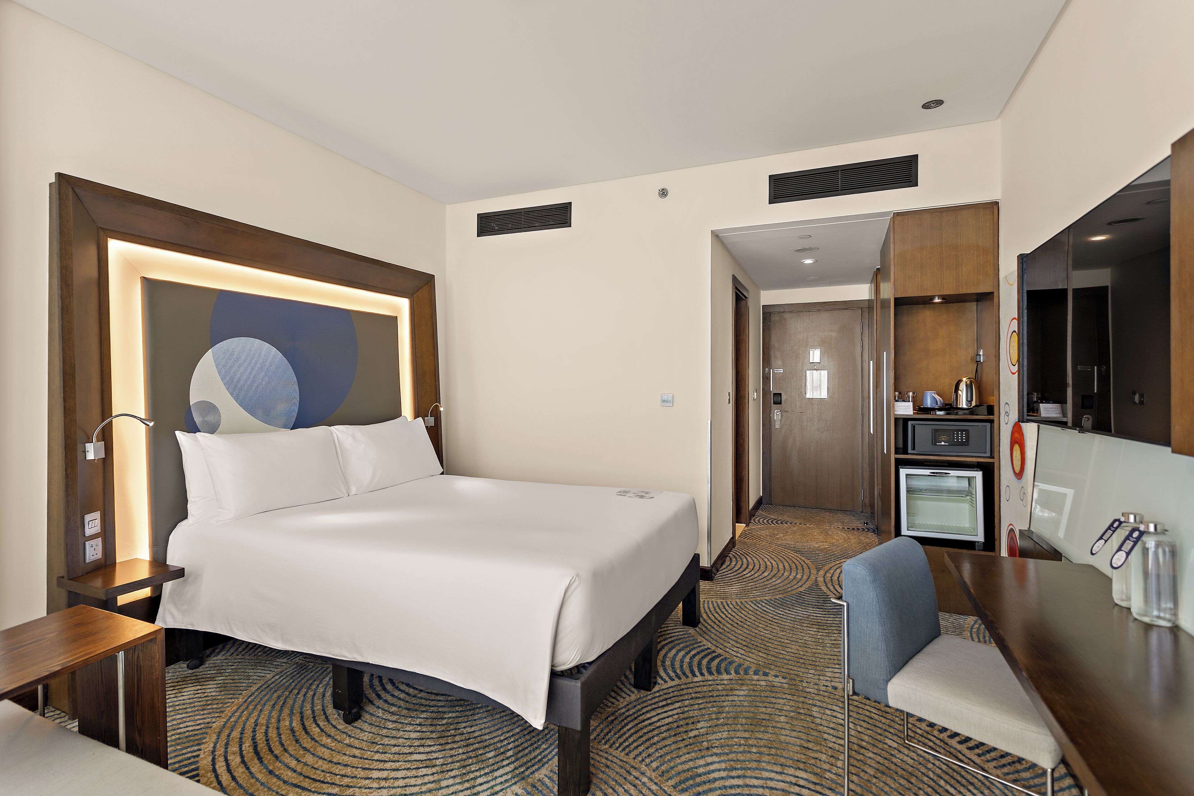 Habitación de hotel con cama, escritorio, silla, microondas y una pequeña kitchenette.