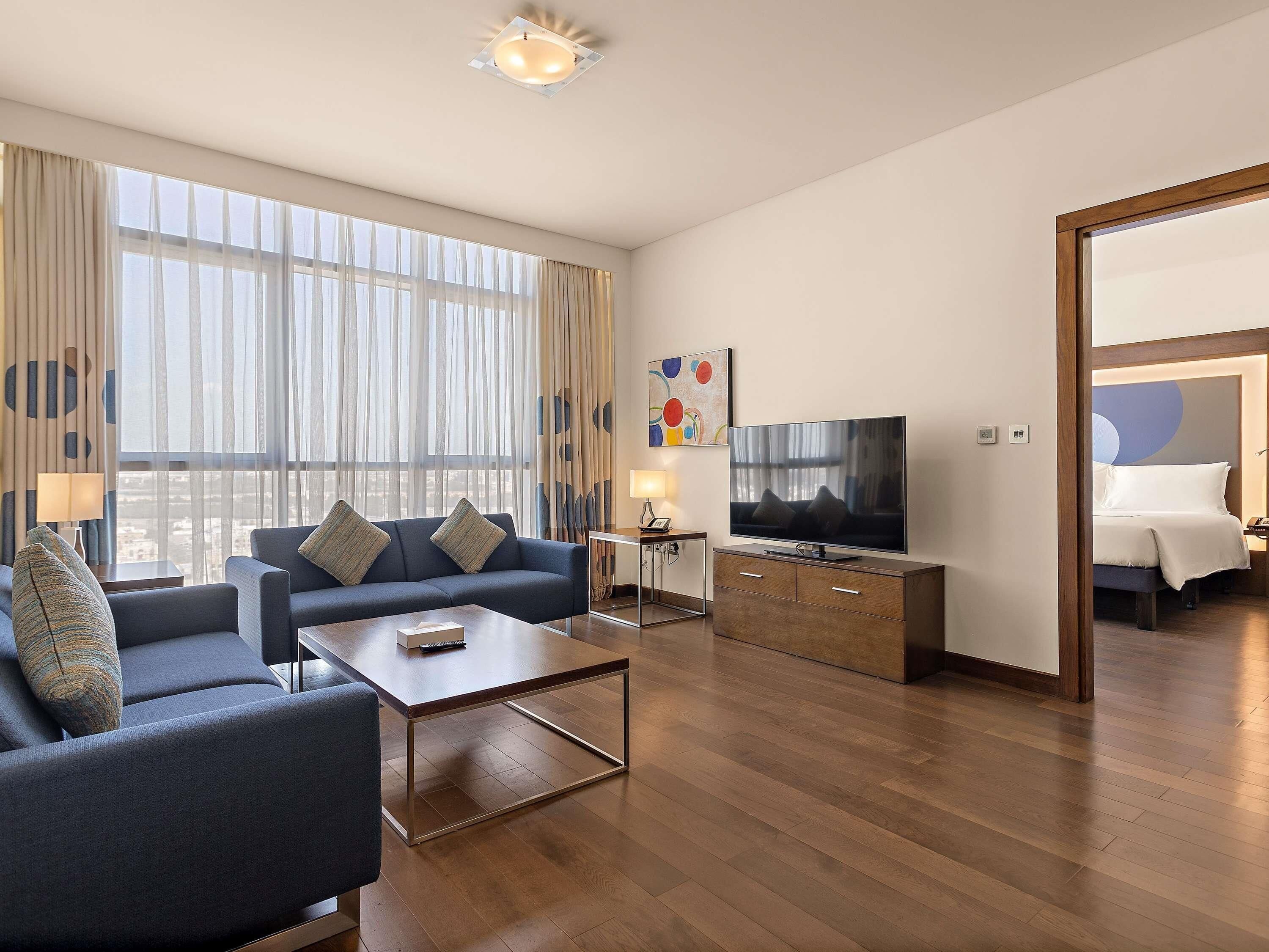A modern hotel room with a sofa, coffee table, TV, and a bed.