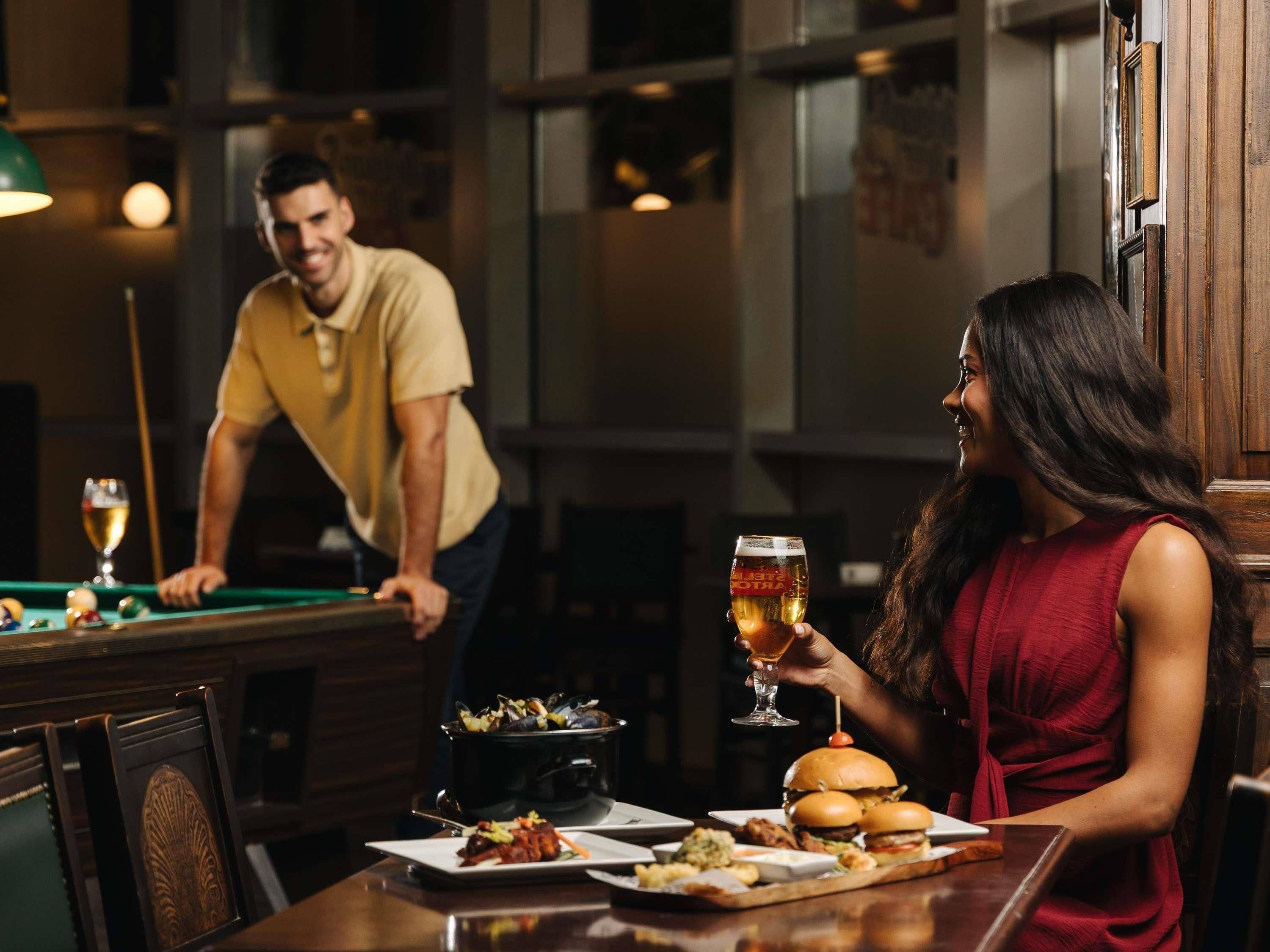 Mesa de billar, mesa de comedor con comida y bebidas, y una zona de bar con billar en una habitación con poca luz.