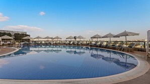 Une grande piscine intérieure, dotée de chaises longues et de parasols, et entourée d’une terrasse carrelée.