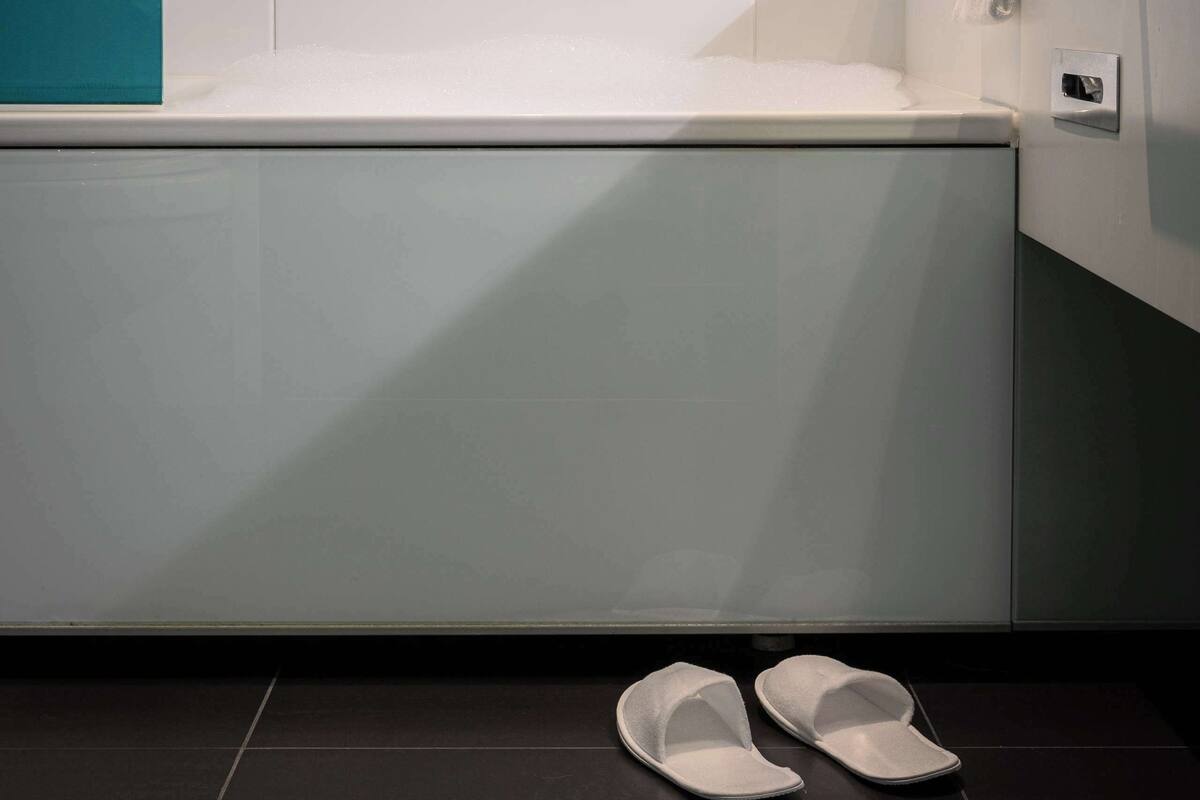 A bathroom with a bathtub, a towel rack, and a pair of slippers on the floor.