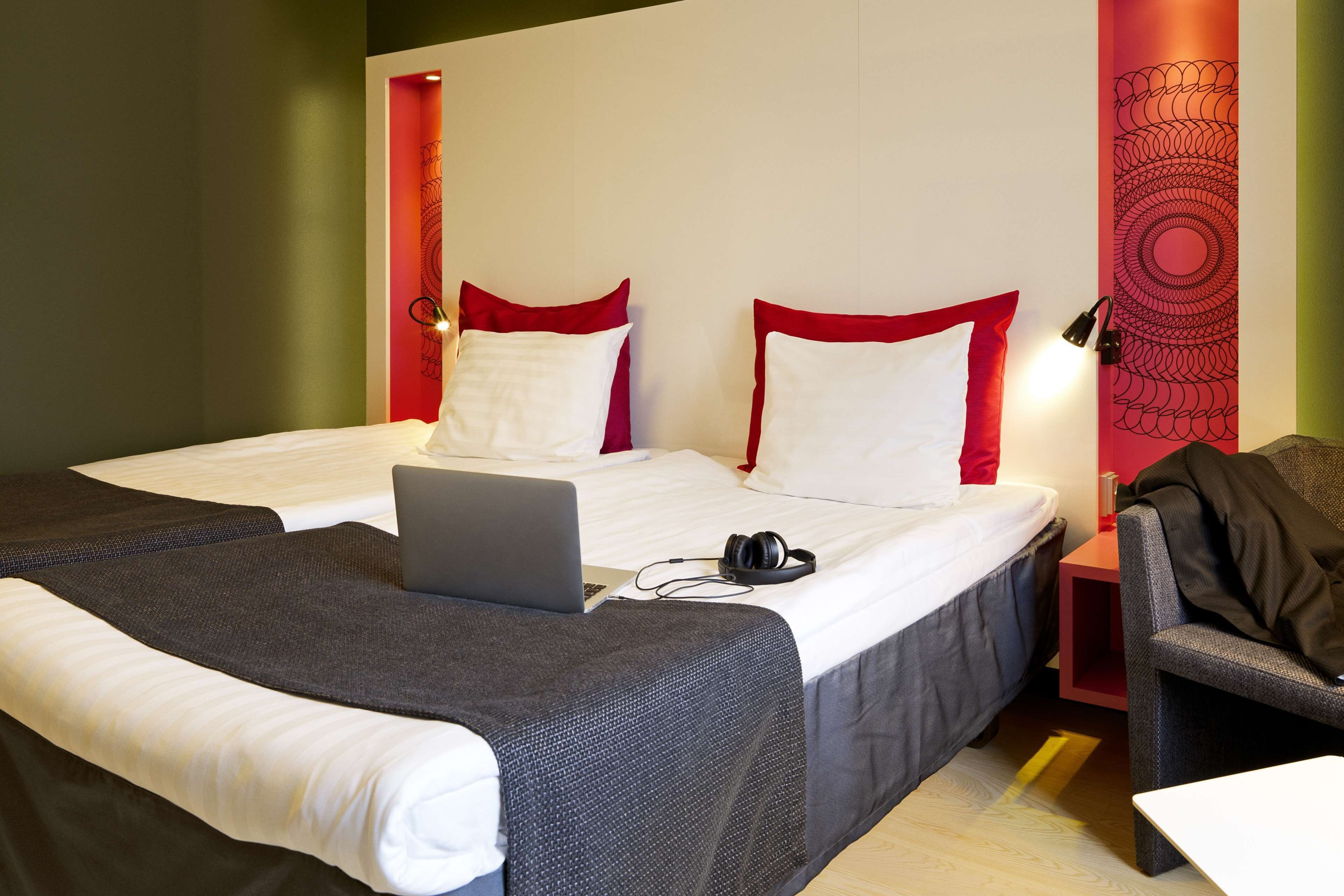 Hotellihuone, jossa on kaksi sänkyä, kannettava tietokone, kuulokkeet ja tuoli.