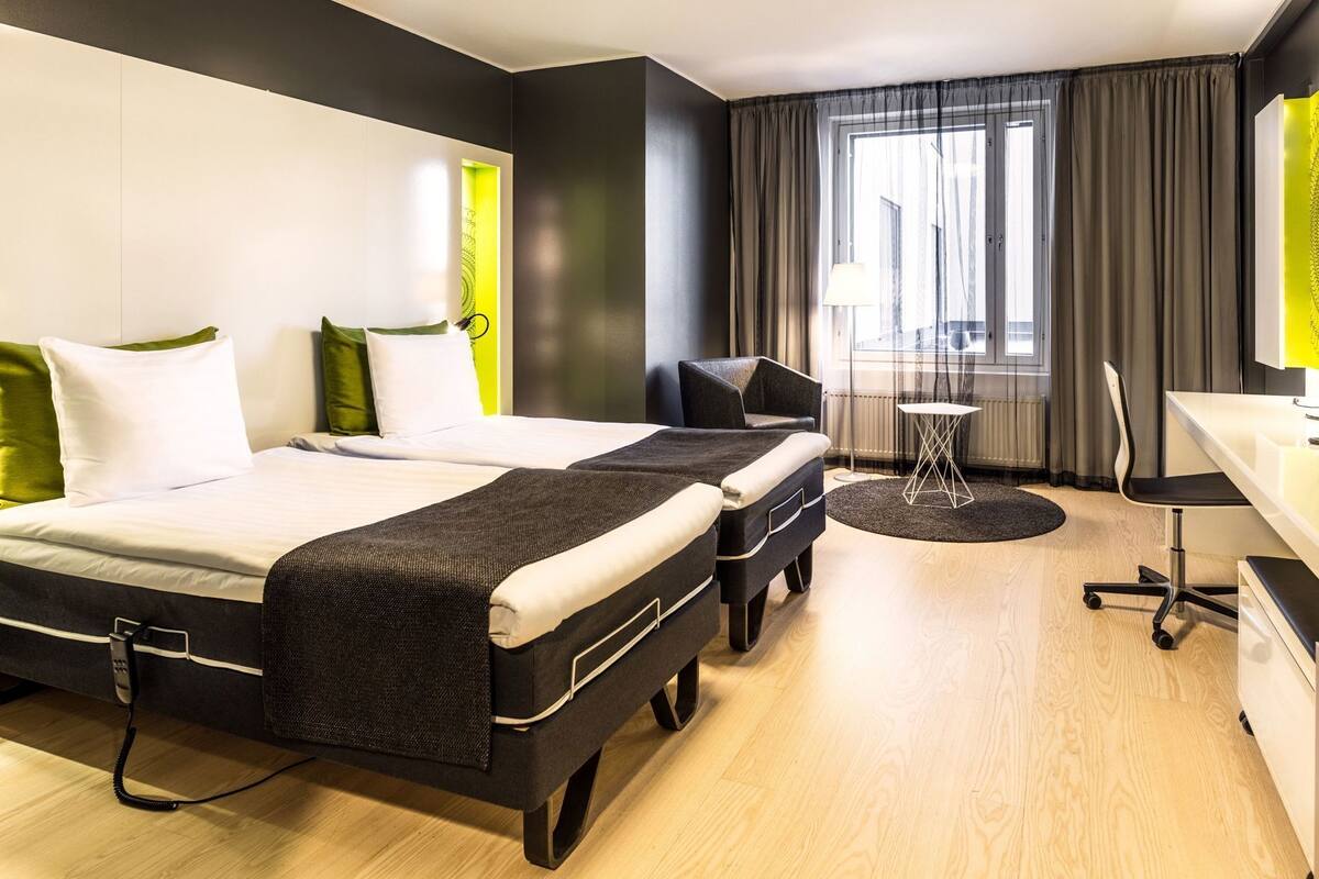 A modern hotel room with a bed, two bedside tables, a desk, and a chair.