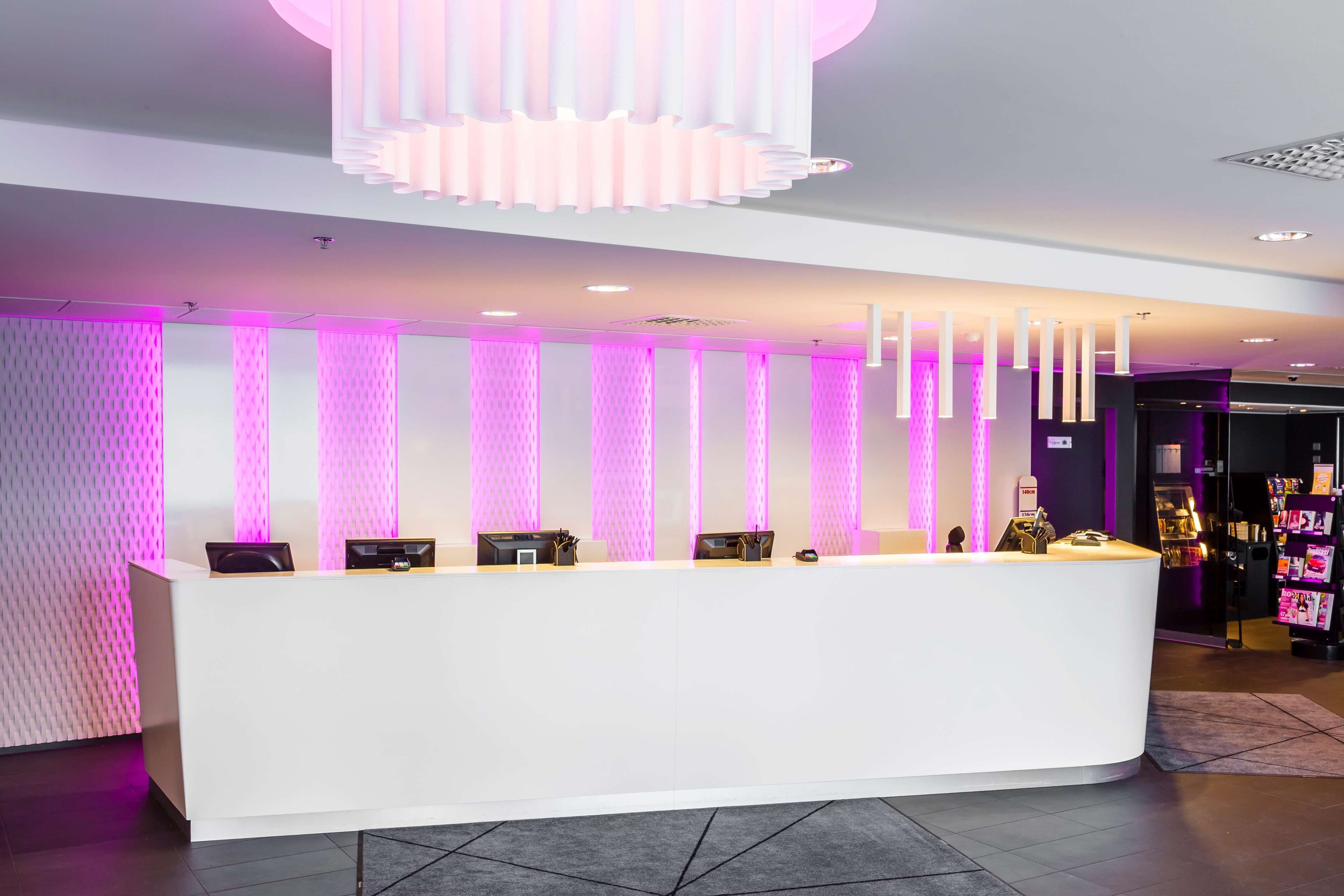 A modern reception desk with a white counter, multiple computer stations, and a patterned wall.